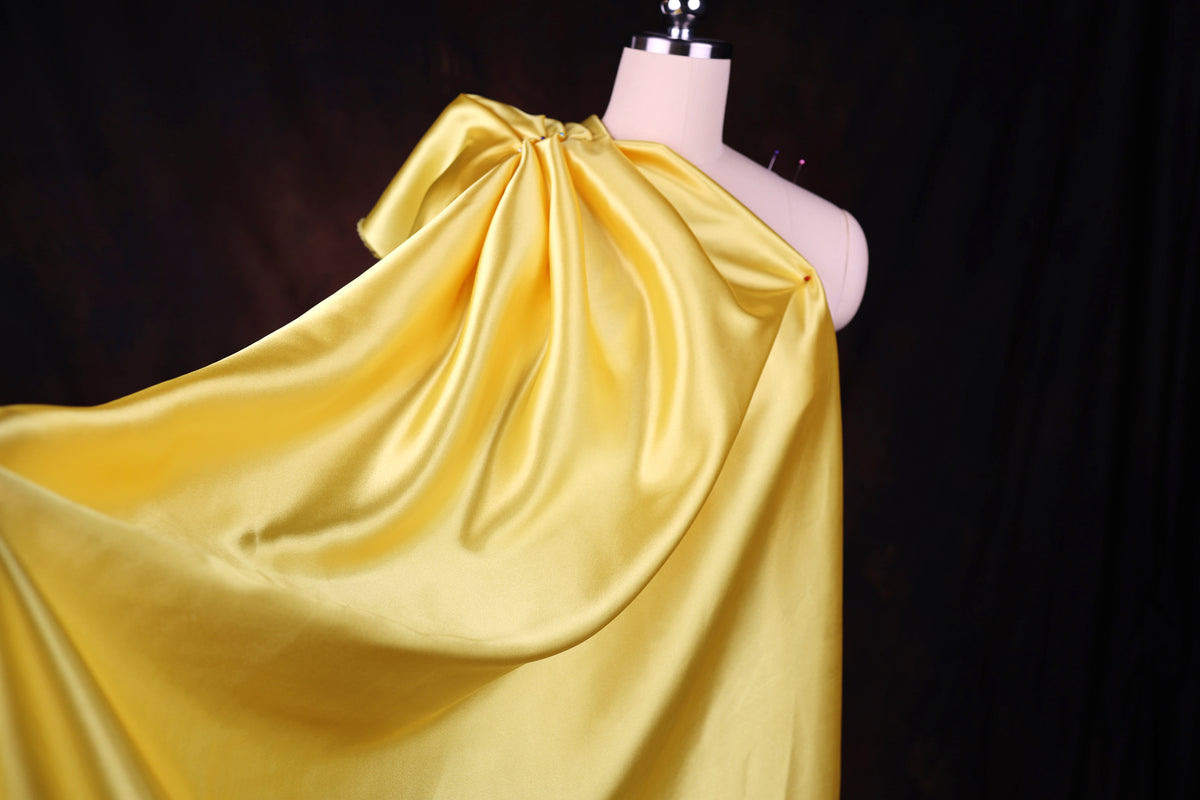 A mannequin wearing a yellow satin one-shoulder dress with a flowing, draped design.