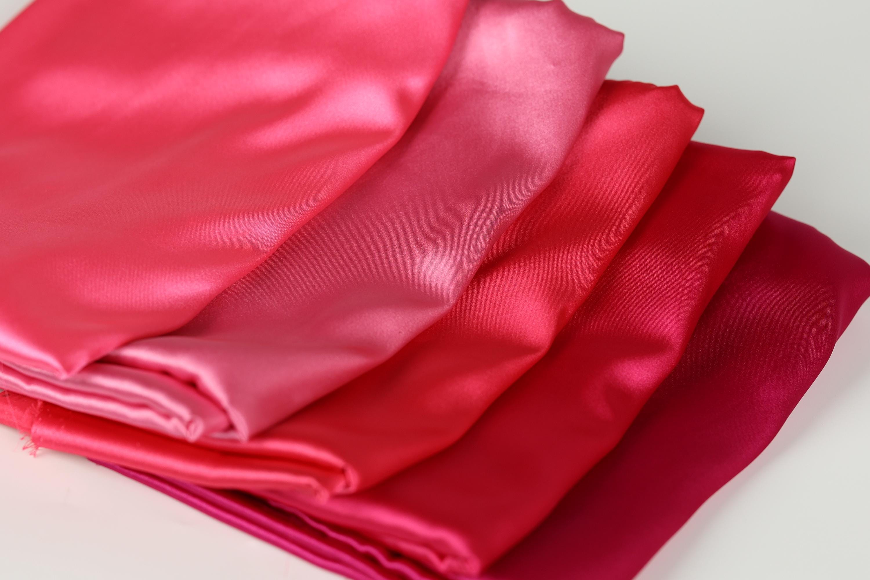 A close-up image of a pile of fabric in various shades of pink, ranging from a bright, vibrant color to a more subdued, muted tone.