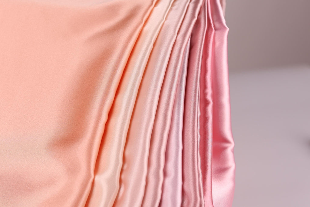 A close-up view of a soft, flowing fabric with a gradient of pink to peach colors, creating a visually appealing and textured appearance.