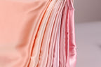 A close-up view of a soft, flowing fabric with a gradient of pink to peach colors, creating a visually appealing and textured appearance.