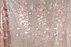 a close-up view of a fabric with a delicate floral pattern, including pink and white flowers and leaves. The fabric appears to be made of sequin material, adding a sparkly texture to the overall design.