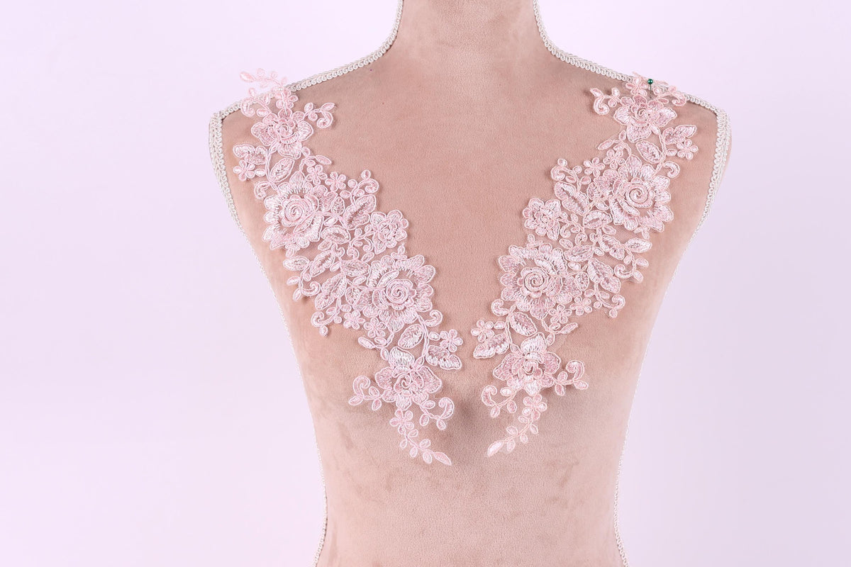 A mannequin wearing a pink lace dress with intricate floral patterns on the shoulders and neckline.