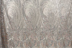 a close-up view of a fabric with a repeating pattern of silver and pink sequin designs. The pattern consists of various shapes and sizes of sequins arranged in a decorative manner, creating a visually striking and intricate design.