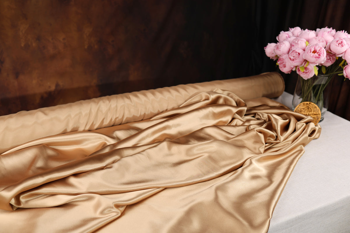 a luxurious gold satin fabric draped over a table, with a vase of pink flowers placed next to it.