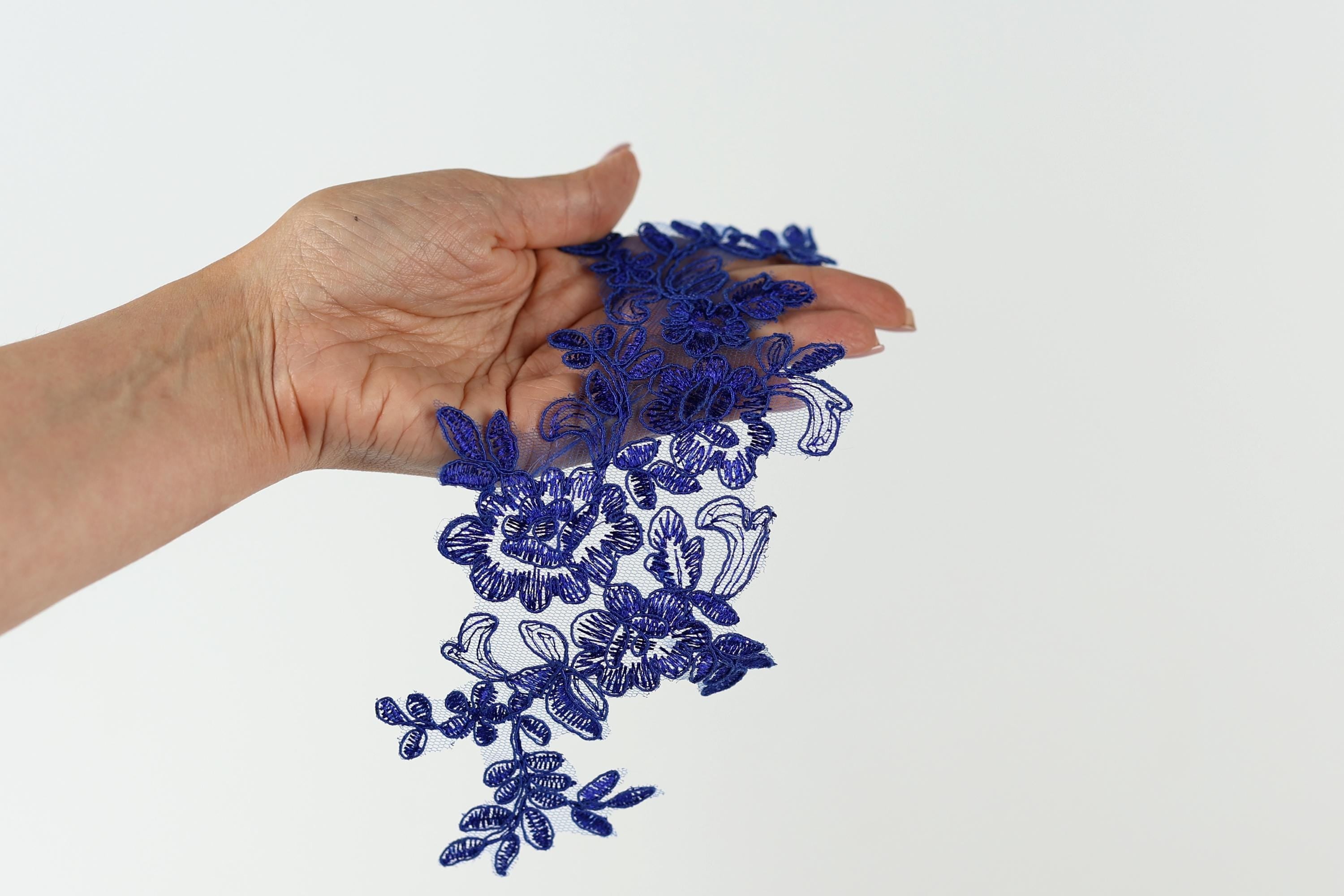 A hand holding a cluster of blue lace or embroidery pieces.