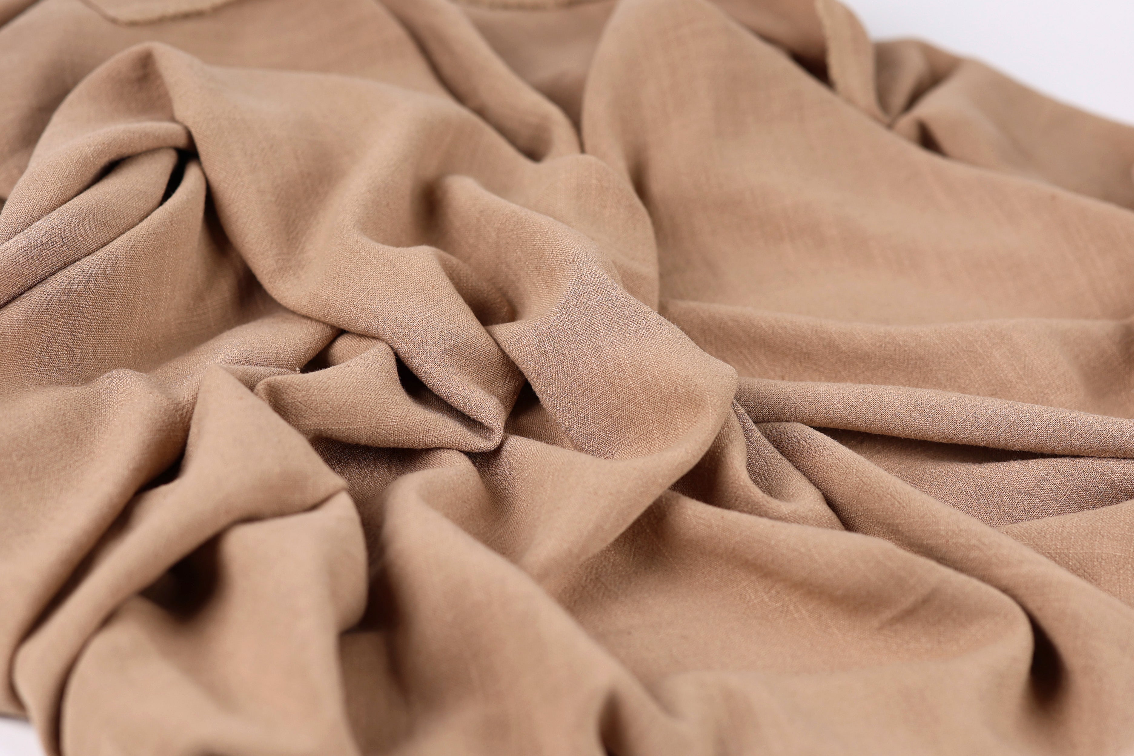 A close-up image of a crumpled, light brown fabric, possibly a piece of clothing or textile.