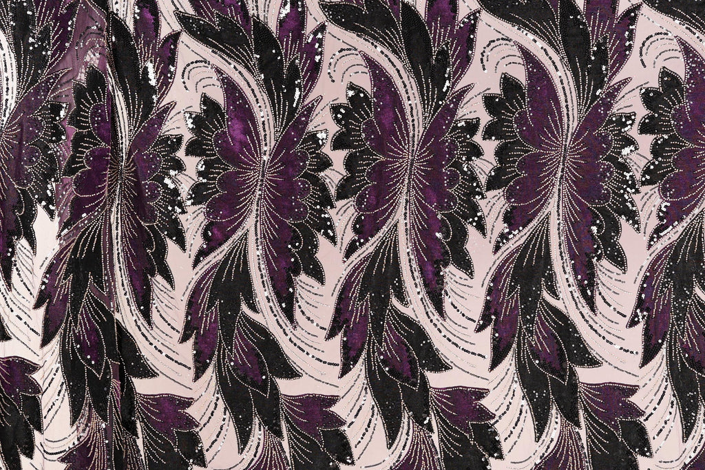 a close-up view of a fabric with a repeating floral pattern in shades of purple and black. The pattern consists of stylized flowers and leaves, creating a visually striking and intricate design. The fabric appears to be made of a material with a metallic or sequined texture, adding a touch of sparkle and elegance to the overall appearance.