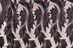 a close-up view of a fabric with a repeating floral pattern in shades of purple and black. The pattern consists of stylized flowers and leaves, creating a visually striking and intricate design. The fabric appears to be made of a material with a metallic or sequined texture, adding a touch of sparkle and elegance to the overall appearance.