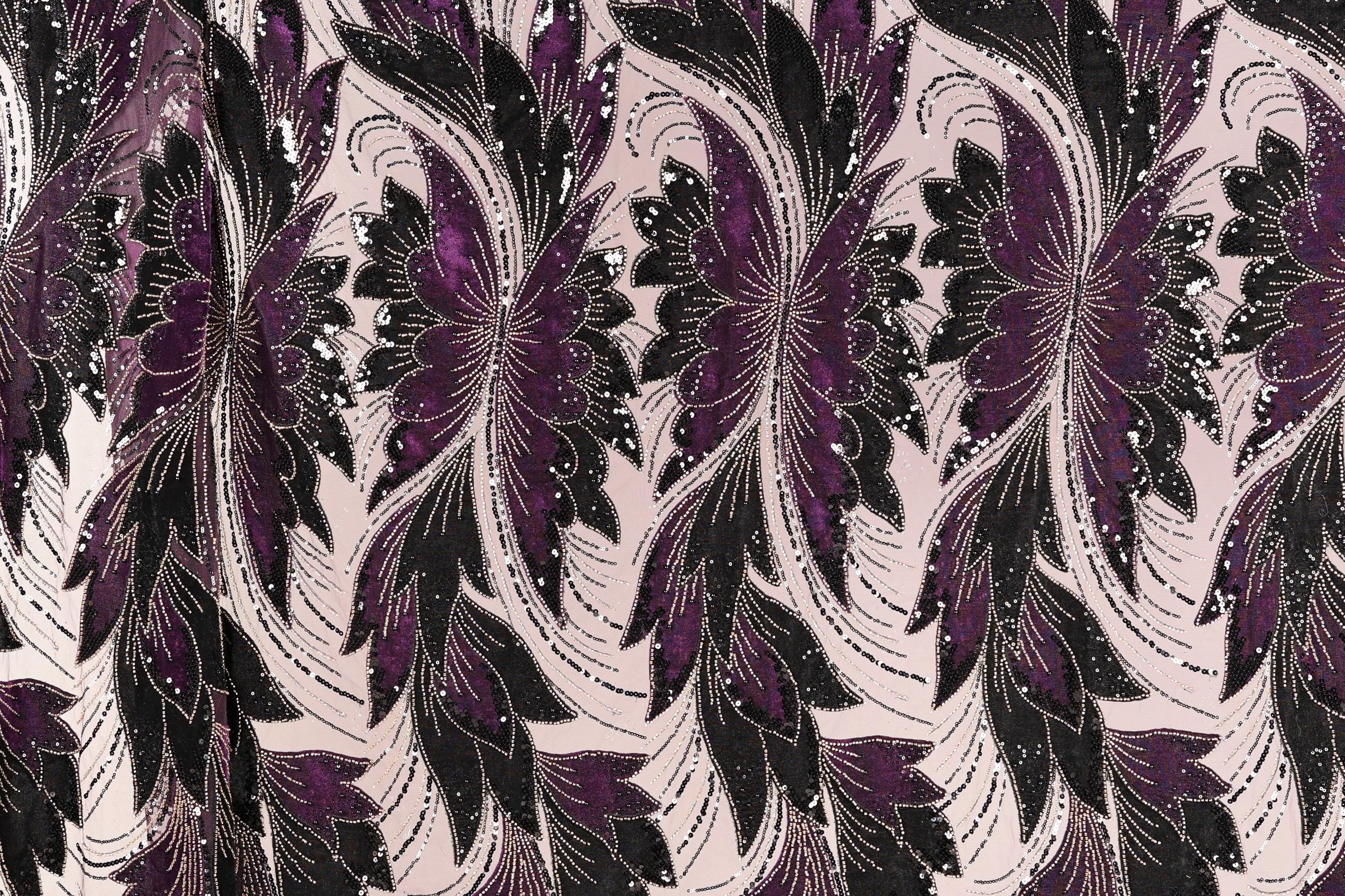 a close-up view of a fabric with a repeating floral pattern in shades of purple and black. The pattern consists of stylized flowers and leaves, creating a visually striking and intricate design. The fabric appears to be made of a material with a metallic or sequined texture, adding a touch of sparkle and elegance to the overall appearance.