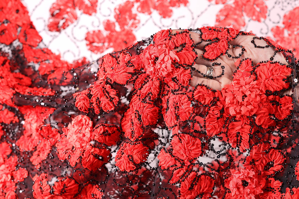 The image is a close-up of a fabric with a red and black floral pattern, featuring numerous small red flowers and black beads or sequins.