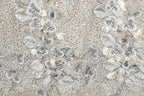 a close-up view of a fabric with a floral pattern. The fabric appears to be made of a material with a silver or metallic sheen, and it is adorned with numerous small white flowers and leaves. The pattern is intricate and detailed, showcasing the craftsmanship and artistry involved in creating the fabric.