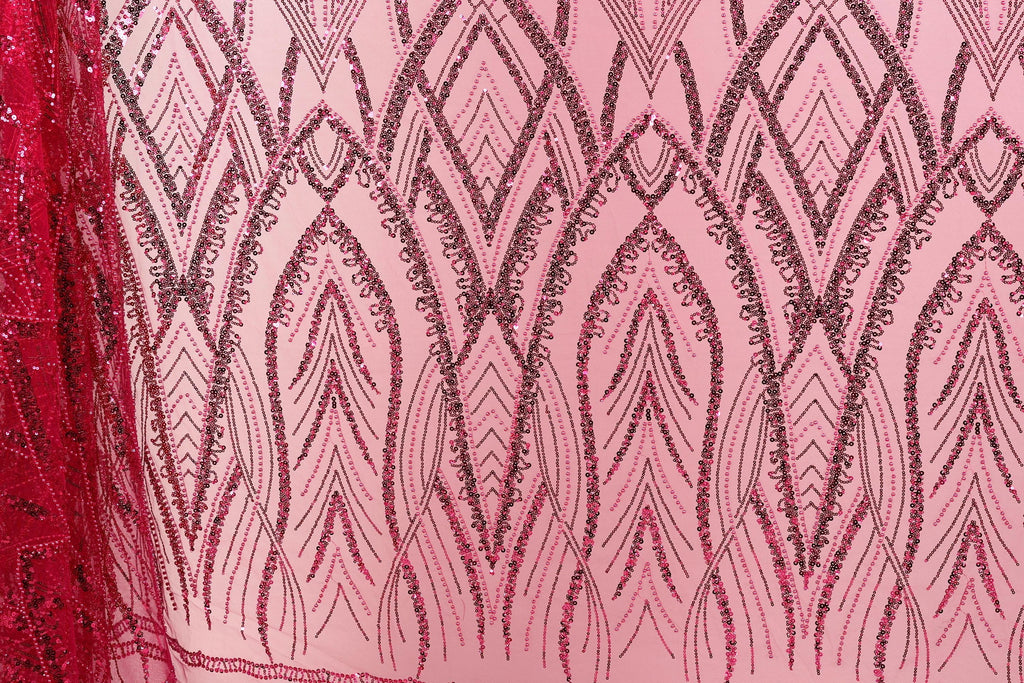 a close-up view of a fabric with a pink background and a repeating pattern of black and red sequin designs. The pattern consists of various shapes and lines, creating a visually striking and intricate design.