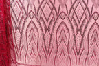 a close-up view of a fabric with a pink background and a repeating pattern of black and red sequin designs. The pattern consists of various shapes and lines, creating a visually striking and intricate design.