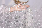 A hand is holding a piece of sheer, white fabric with a silver leaf pattern.