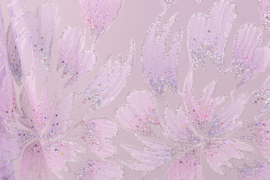 a close-up view of a patterned fabric with a floral design. The fabric has a pink and purple color scheme, and the pattern includes various shapes and textures, such as leaves, flowers, and other organic elements. The image does not contain any text or countable objects, and the focus is on the intricate and visually appealing design of the fabric.