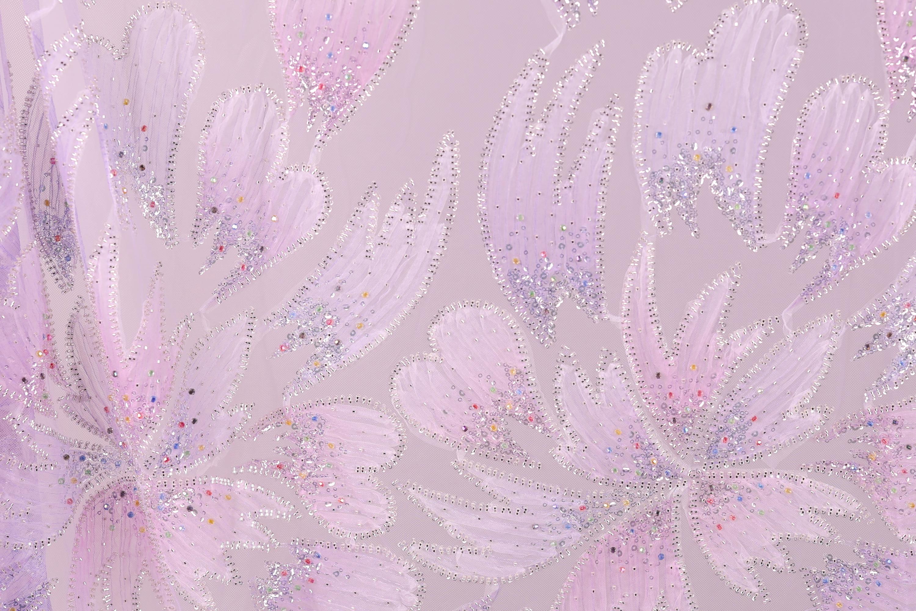 a close-up view of a patterned fabric with a floral design. The fabric has a pink and purple color scheme, and the pattern includes various shapes and textures, such as leaves, flowers, and other organic elements. The image does not contain any text or countable objects, and the focus is on the intricate and visually appealing design of the fabric.