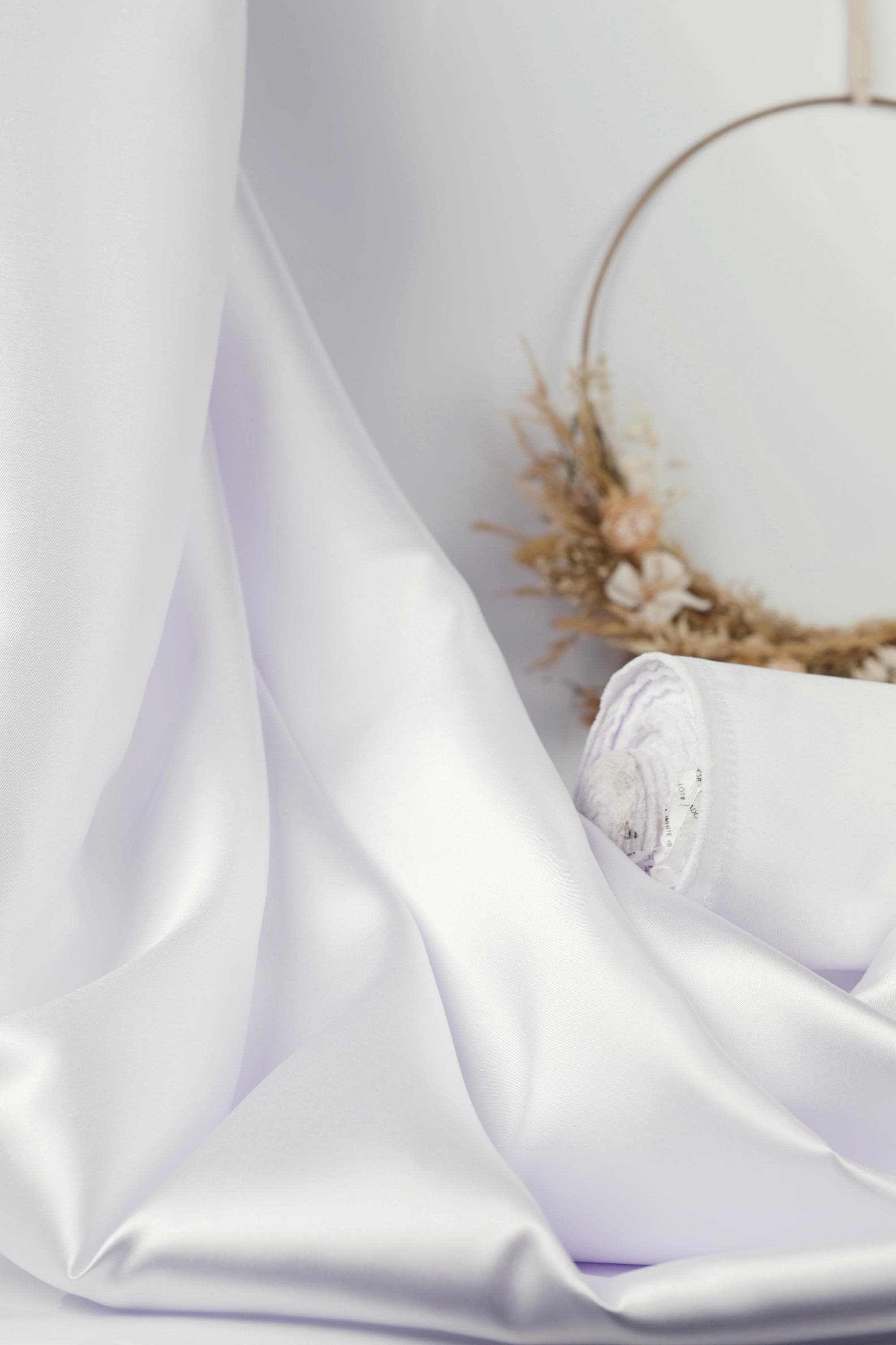 a white fabric draped over a surface, with a wreath made of dried flowers and a white circular object in the background.