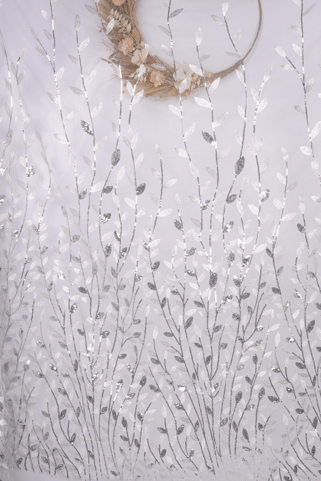 a white fabric with a repeating pattern of silver and white leaves and flowers, creating a delicate and intricate design.