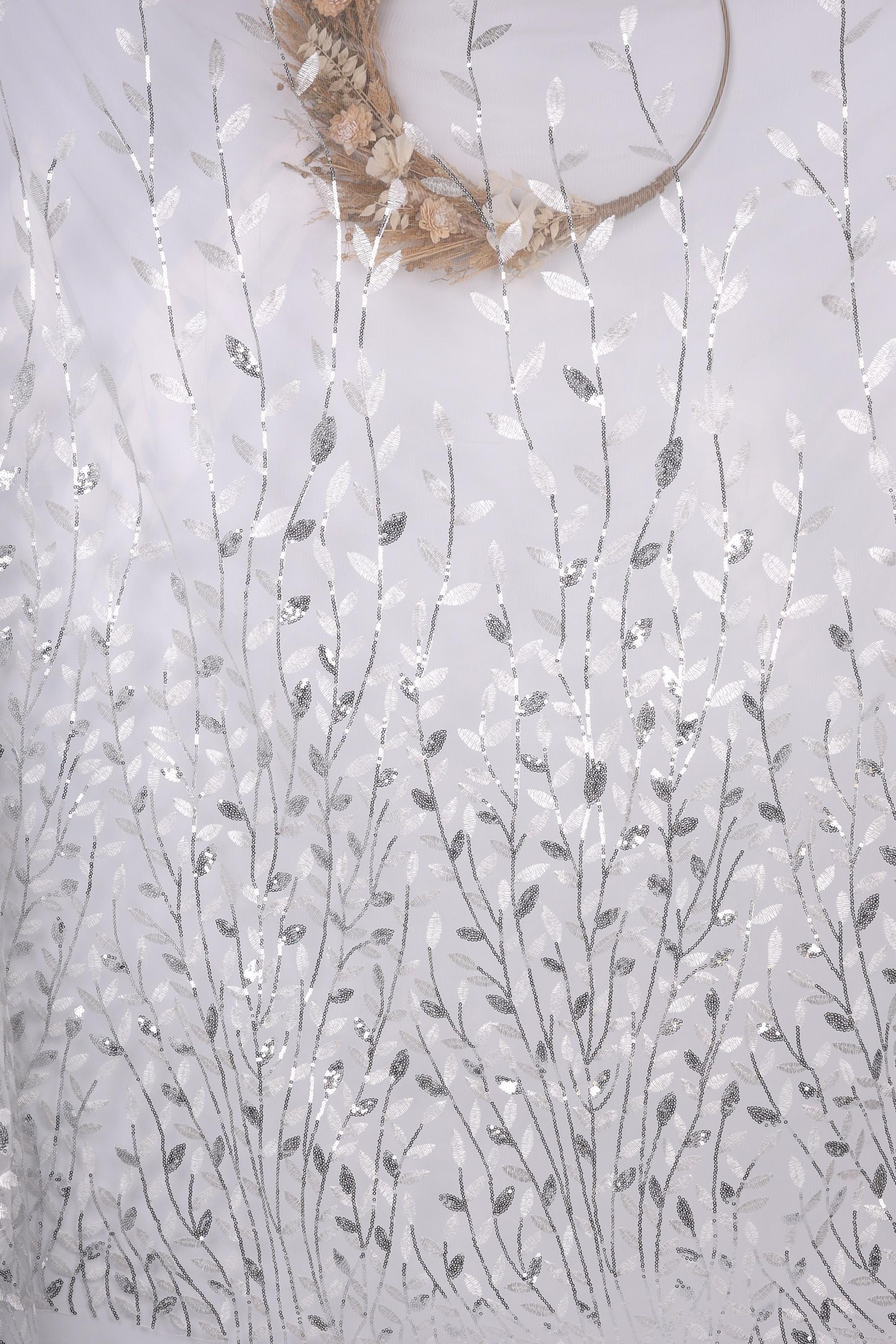 a white fabric with a repeating pattern of silver and white leaves and flowers, creating a delicate and intricate design.