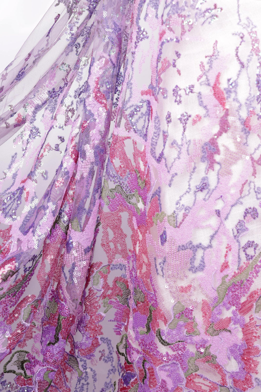 a close-up view of a fabric with a vibrant, multicolored floral pattern. The fabric appears to be made of a sheer material, with a mix of pink, purple, and green colors. The pattern is intricate and detailed, showcasing the craftsmanship and artistry of the fabric design.