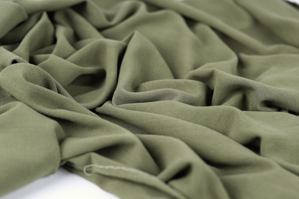 a close-up view of a crumpled, olive green fabric, with its folds and creases clearly visible.