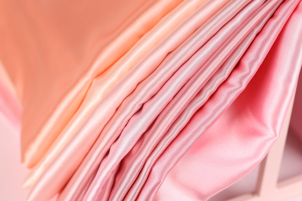 A close-up view of a soft, flowing fabric in shades of pink and peach, with a subtle gradient effect.