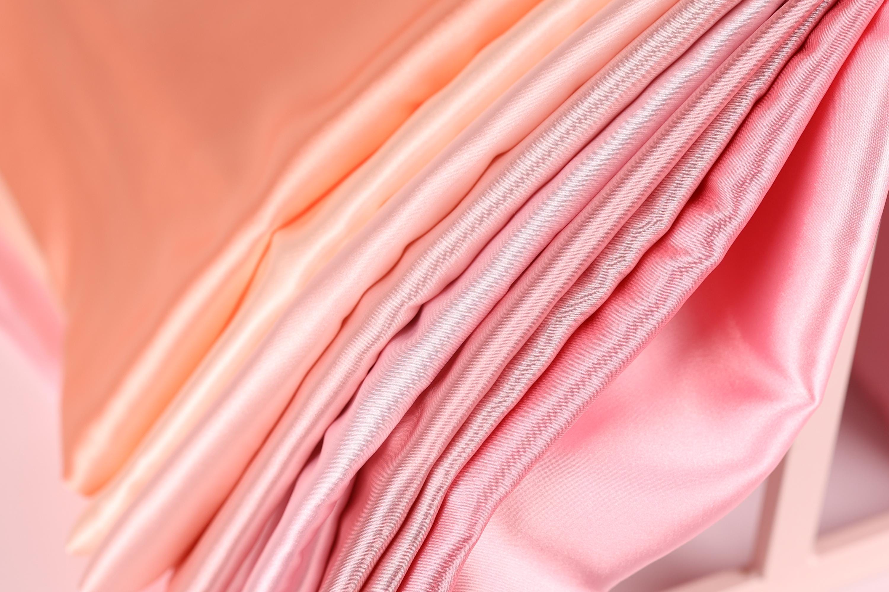 A close-up view of a soft, flowing fabric in shades of pink and peach, with a subtle gradient effect.