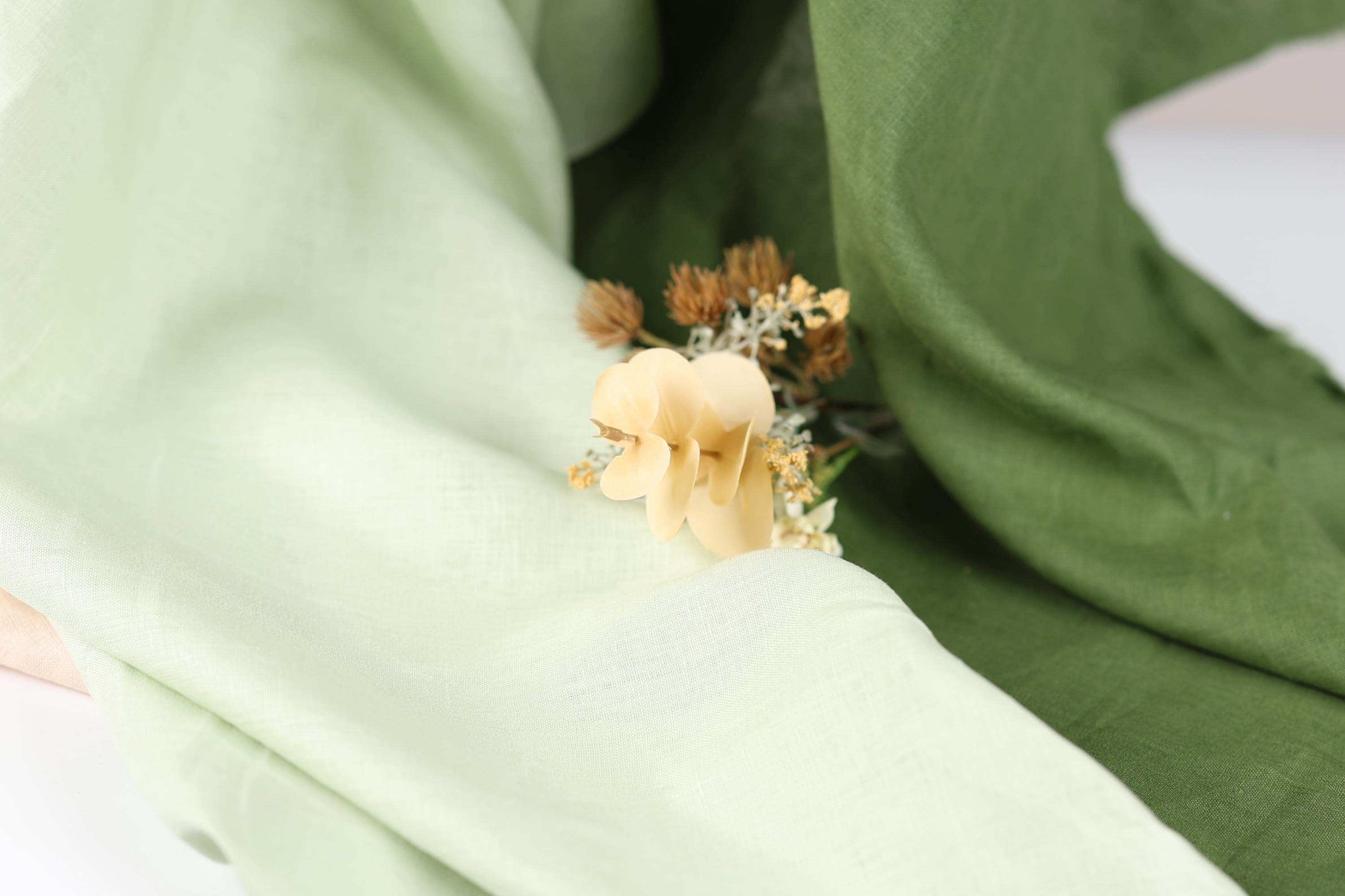 A close-up view of a delicate yellow flower resting on a green fabric, with the fabric partially visible in the background.
