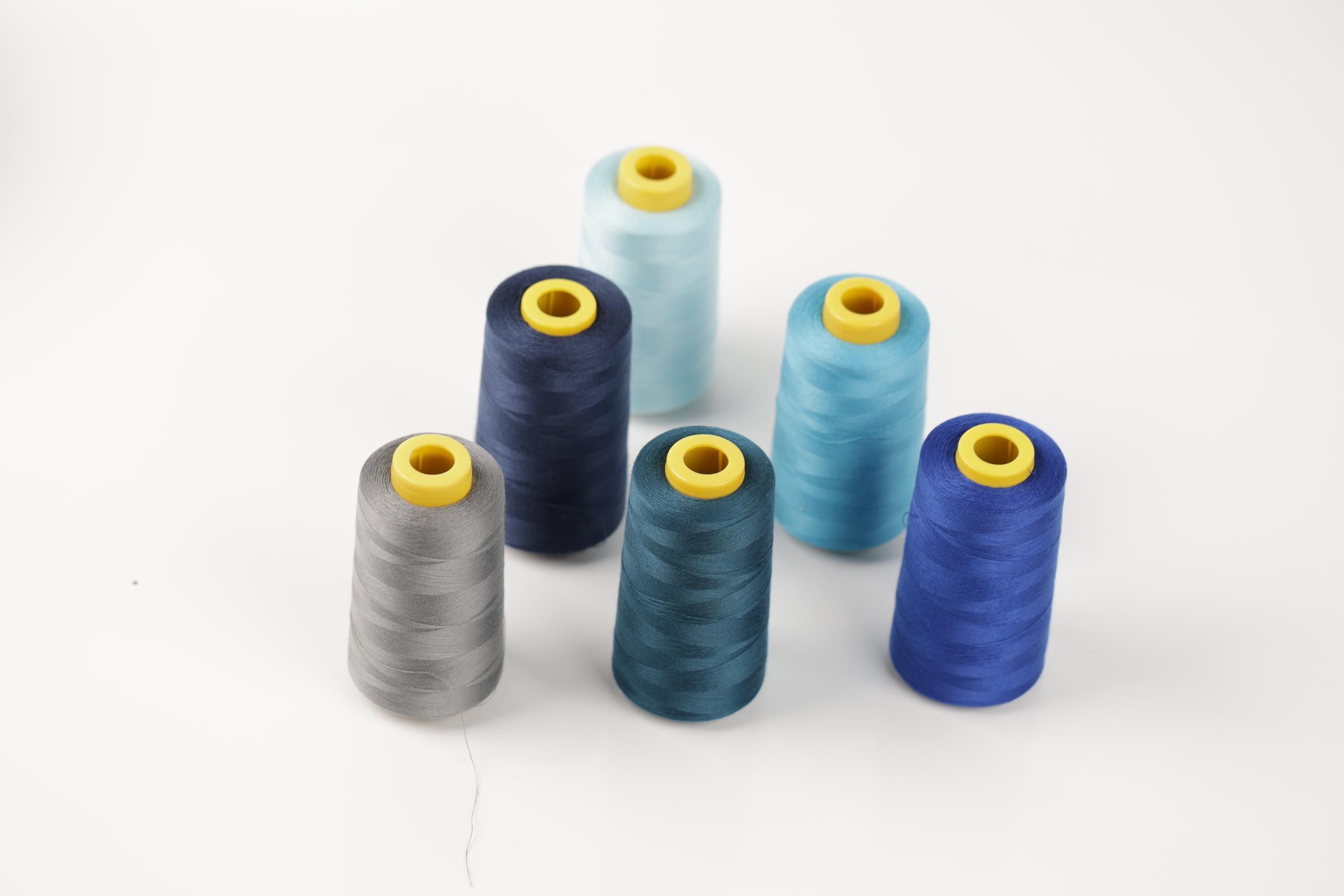 A group of six spools of thread in various colors, including blue, gray, and teal, arranged on a white background.