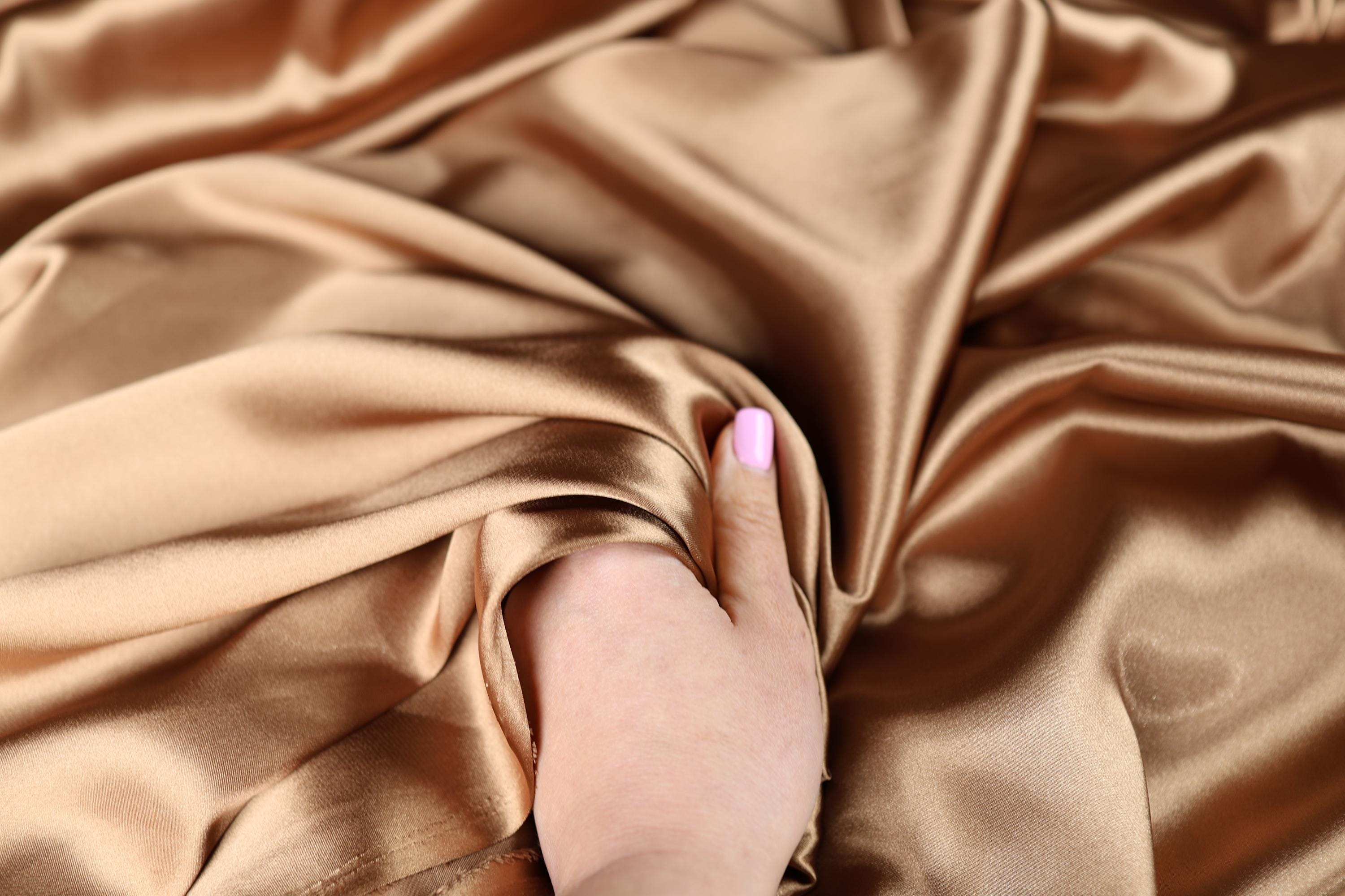 a woman&#39;s hand with a pink manicure resting on a satin fabric