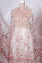 A mannequin wearing a white dress with a sheer, floral-patterned fabric draped over it.