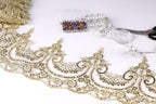a close-up view of a decorative gold lace trim, with a spool of thread, a box of sewing pins, and a pair of scissors on a white background.
