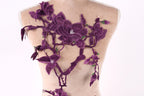 a mannequin with a back adorned with a floral design in shades of purple. The design consists of purple flowers and leaves, creating a visually striking and intricate pattern.