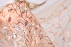 a close-up view of a delicate, peach-colored fabric with a floral pattern. The fabric appears to be made of sheer material, with a subtle shimmering effect due to the presence of sequins or glitter. The background is blurred, drawing focus to the fabric and its intricate design.