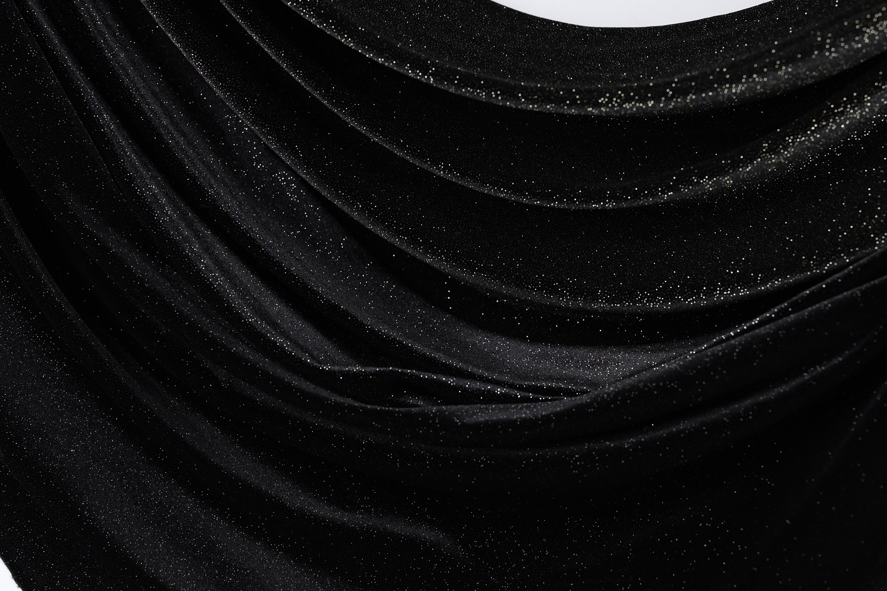 The image is a close-up of a shiny black fabric with a sparkling texture, creating a visually striking contrast.