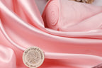 a close-up view of a pink satin fabric, with a sewing artisan's label prominently displayed in the foreground.