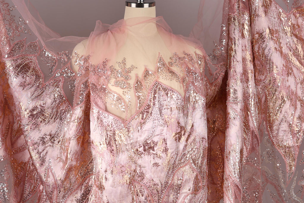 a pink and gold sequined dress with a sheer, lace-like texture. The dress appears to be made of sheer fabric, giving it a delicate and elegant appearance. The sequins and lace-like texture add a touch of sparkle and sophistication to the overall design.