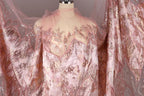 a pink and gold sequined dress with a sheer, lace-like texture. The dress appears to be made of sheer fabric, giving it a delicate and elegant appearance. The sequins and lace-like texture add a touch of sparkle and sophistication to the overall design.