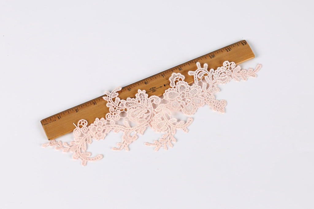 a delicate lace piece with intricate floral patterns lying on a wooden ruler, which is placed on a plain white background.