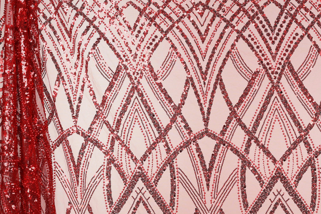 a close-up view of a fabric with a repeating pattern of red and black sequin designs. The pattern consists of diagonal lines and arches, creating a visually striking and intricate design. The fabric appears to be a pink background with the red and black sequin designs covering the entire surface.