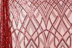 a close-up view of a fabric with a repeating pattern of red and black sequin designs. The pattern consists of diagonal lines and arches, creating a visually striking and intricate design. The fabric appears to be a pink background with the red and black sequin designs covering the entire surface.