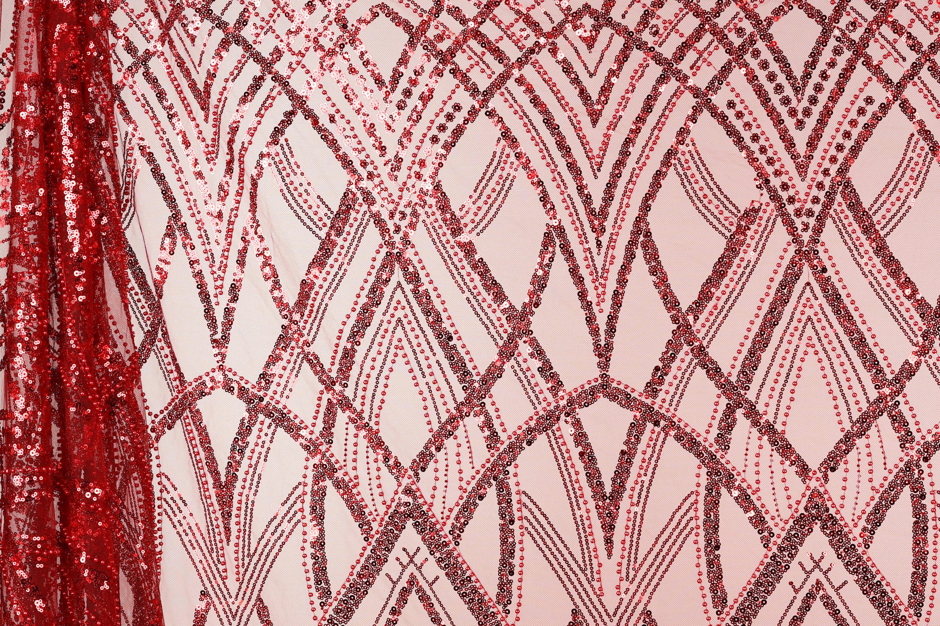 a close-up view of a fabric with a repeating pattern of red and black sequin designs. The pattern consists of diagonal lines and arches, creating a visually striking and intricate design. The fabric appears to be a pink background with the red and black sequin designs covering the entire surface.