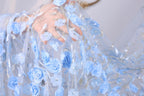 A close-up view of a hand holding a delicate, intricately embroidered fabric with blue flowers and silver embellishments.