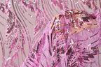 A close-up view of a hand holding a piece of pink and purple sequin fabric, with the fabric's intricate patterns and textures visible.