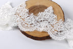 A close-up image of a delicate white lace fabric, possibly a bridal veil or headband, resting on a wooden surface.