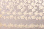 a close-up view of a delicate, intricate lace pattern with a floral design. The lace appears to be made of a fine, delicate material, possibly silk or chiffon, and is adorned with numerous small white flowers or leaves. The pattern is composed of numerous individual flowers or leaves, creating a visually striking and detailed design. The image does not contain any text or other discernible objects, and the focus is solely on the intricate lace pattern.