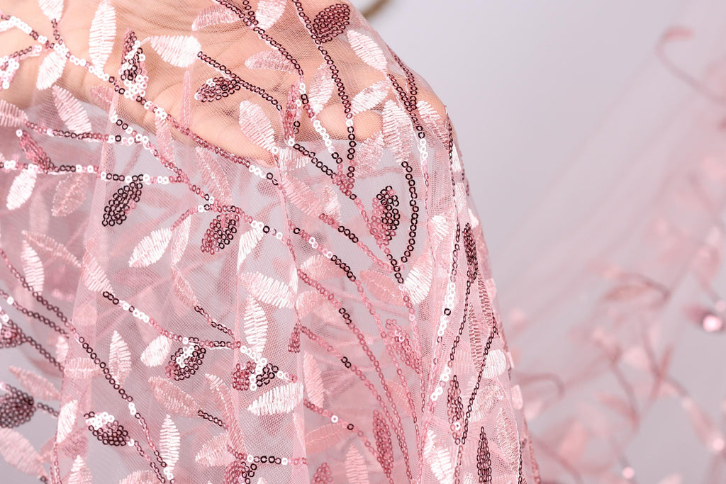 A close-up view of a delicate, pink lace fabric with a floral pattern.