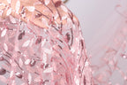 A close-up view of a delicate, pink lace fabric with a floral pattern.