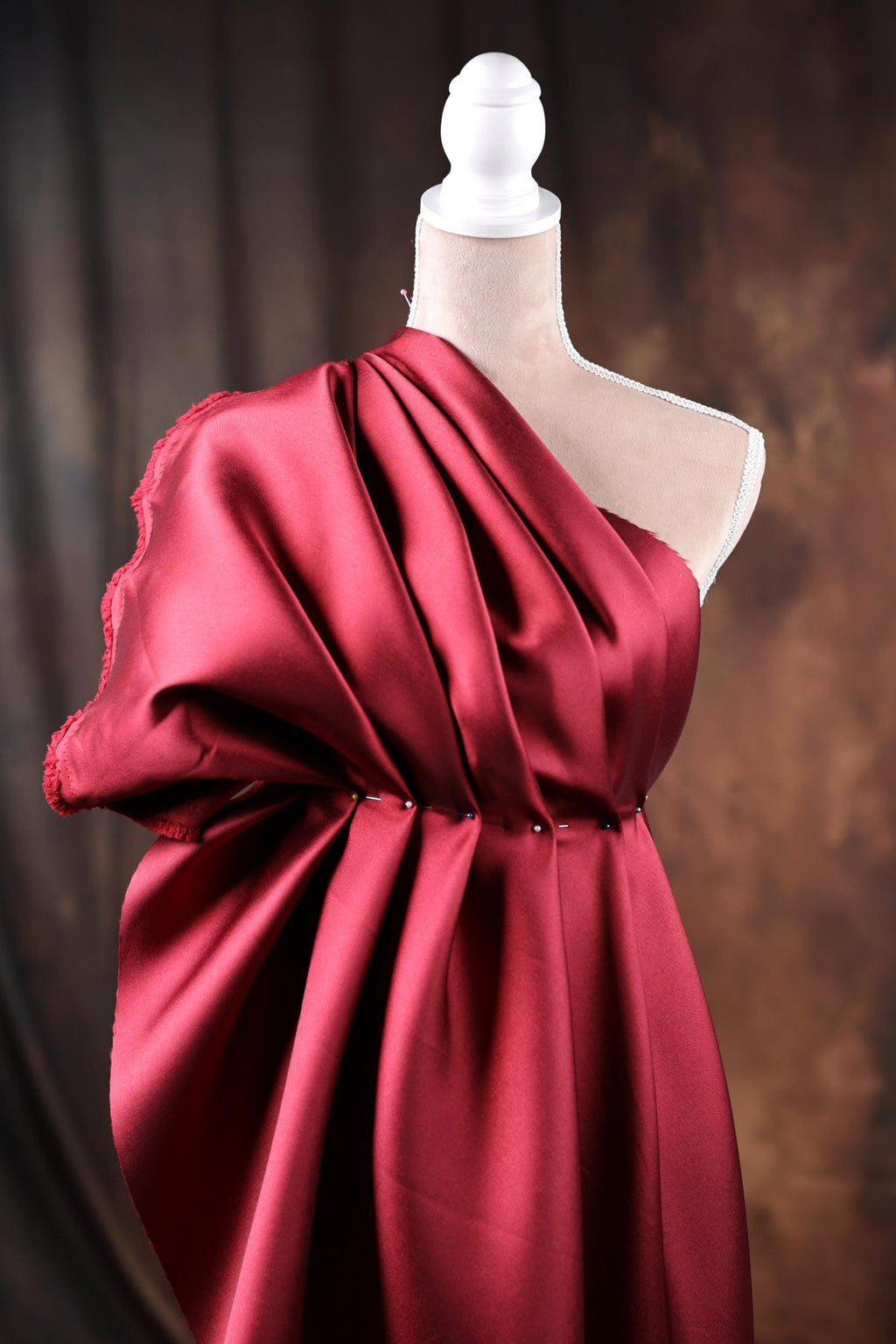 A red, one-shoulder dress displayed on a mannequin, with a dark background.
