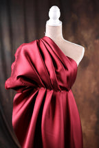 A red, one-shoulder dress displayed on a mannequin, with a dark background.
